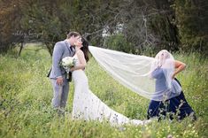 a bride and groom kissing in the middle of a field with their veil blowing in the wind