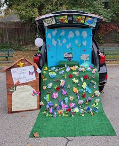 the back end of a car decorated with paper flowers and butterflies, next to a small dog house