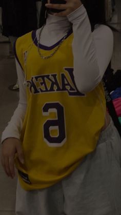 a woman in a lakers jersey taking a selfie with her cell phone while standing next to other people