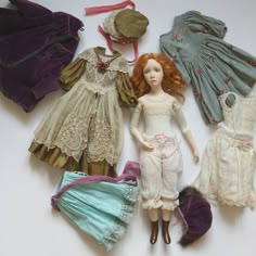 an assortment of dolls and clothes laid out on a white surface with one doll in the middle