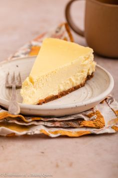 a piece of cheesecake on a plate with a fork and cup in the background