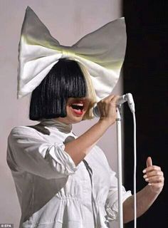 a woman with a white bow on her head singing into a microphone