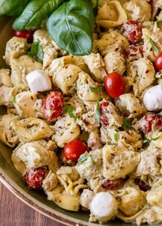 a bowl filled with pasta and vegetables on top of a wooden table next to basil leaves