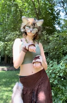 a woman wearing a cat mask and skirt with her hands in the air while standing next to trees