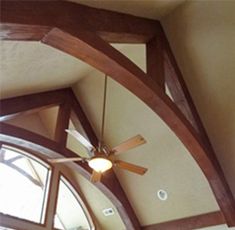 a ceiling fan mounted to the side of a wooden beam in a room with vaulted ceilings