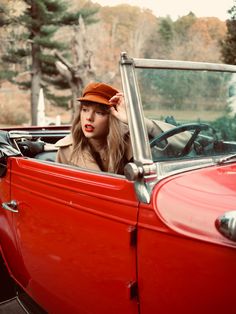 a woman sitting in the driver's seat of an old fashioned red convertible car