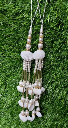 two necklaces with shells and pearls hanging from grass