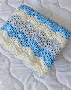 a crocheted blanket laying on top of a bed next to a white pillow