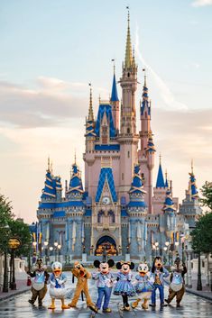 some people are standing in front of a castle with goofy and mickey mouse costumes on