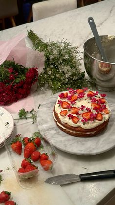 a cake with strawberries on it sitting on a table next to flowers and utensils