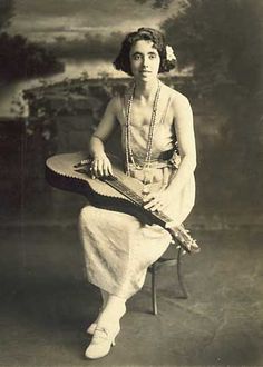 an old photo of a woman sitting on a chair holding a musical instrument in her hands