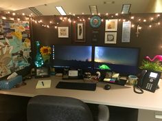 an office desk with two computer monitors and a phone on it, surrounded by string lights