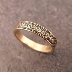 a gold wedding ring with filigrees and scrolls on the outside, sitting on a stone surface