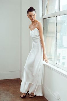 a woman in a white dress leaning against a window