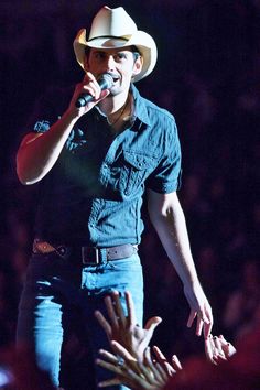 a man wearing a cowboy hat singing into a microphone with his hands in the air