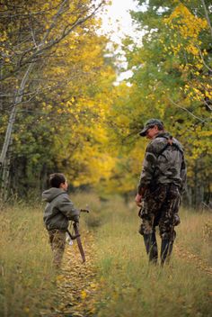 a man and boy are walking through the woods with their hunting gear in hand as they look at each other