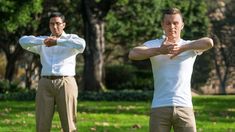 two men in white shirts and khaki pants doing yoga exercises on the grass