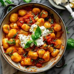 a pan filled with tomatoes and cheese on top of a table next to bread, spoons and utensils