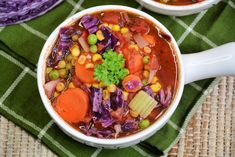 two white bowls filled with vegetable soup on top of a green table cloth next to purple cabbage