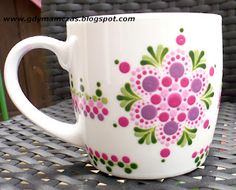 a white coffee cup with pink and green flowers on it sitting on a wicker table