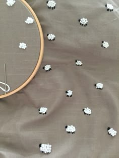 an embroidery project with white and black sheep on grey fabric next to a wooden hoop