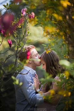 a man and woman are kissing in front of some trees with pink flowers on it