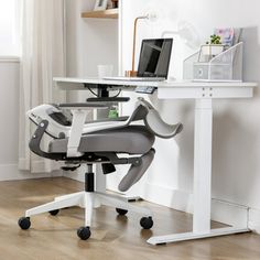 a computer desk with a laptop on top of it next to a white chair in front of a window