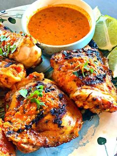 grilled chicken on a plate with dipping sauce and lime wedges next to it