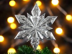 a snowflake ornament hanging from a christmas tree with lights in the background