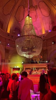 a group of people standing in front of a bar with chandelier hanging from the ceiling