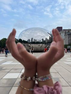 a person holding their hands up in front of a large mirror ball with buildings in the background