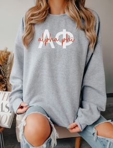 a woman sitting on top of a chair wearing a grey sweatshirt with the word alphha phi printed on it