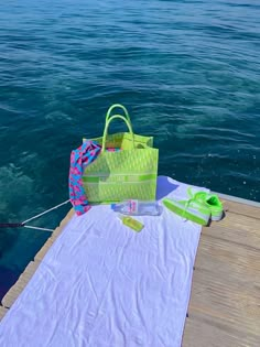 a green bag sitting on top of a white towel next to a body of water