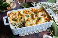 a casserole dish with cheese and spinach on a wooden table next to two wine glasses