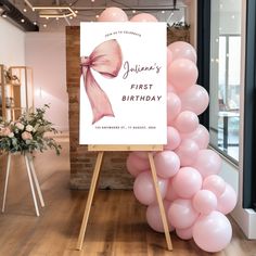 a pink balloon arch with a sign for a first birthday