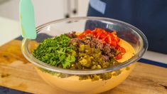 a glass bowl filled with chopped vegetables on top of a wooden cutting board