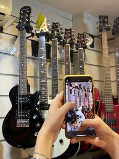 a person holding up a cell phone in front of guitars