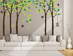 a living room with white couches and green tree decals on the wall behind it