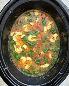 a black crock pot filled with pasta and spinach soup on top of a white table