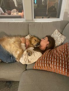 a woman laying on top of a couch next to a dog