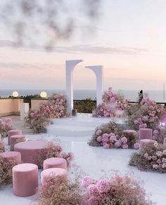 an outdoor wedding setup with pink flowers on the ground and white arches in the background