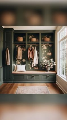 a room with green cabinets and flowers on the wall, two coats hanging from hooks