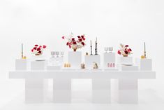 a white table topped with lots of vases filled with red and white flowers next to candles