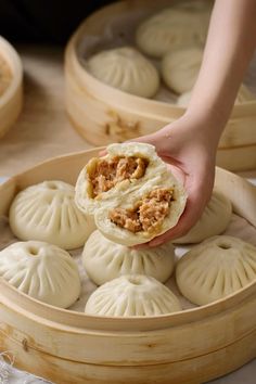 a person is picking up some dumplings out of a wooden container with other dumplings in the background