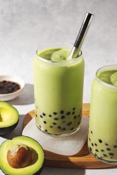 an avocado smoothie in a glass with a straw and two pieces of fruit on the side