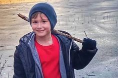 a young boy holding a stick and wearing a blue beanie while standing in the snow