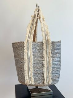 Beach Bag Perfection! The woven straw exterior, adorned with pearl and canvas detailing, and silver color adds a touch of femininity to this structured bag! Throw all of your essentials in this fabulous bag and your ready for a day at the beach / pool! Size info 16” L x 24” H 11" strap drop. Structured silhouette with flat base for stability Paper straw/polyester Beach Tote Bag With Pearl Handle, Chic Straw Bag With Pearl Handle For Vacation, Summer Vacation Straw Bag With Pearl Handle, Summer Shopping Bags With Pearl Handle, Silver Shoulder Bag For Summer Shopping, Silver Shoulder Bag For Summer, Silver Rectangular Shoulder Bag For Summer, Chic Silver Bag For Summer, Chic Silver Bags For Summer