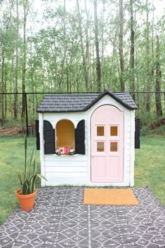 a small dog house with a pink door and window on top of a rug in the yard