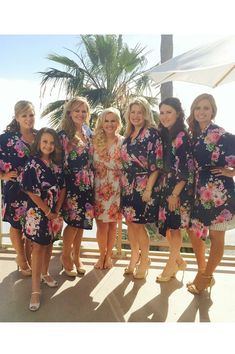 a group of women standing next to each other in front of a palm tree and water