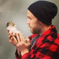 a man in a red and black plaid shirt holding a small animal up to his face